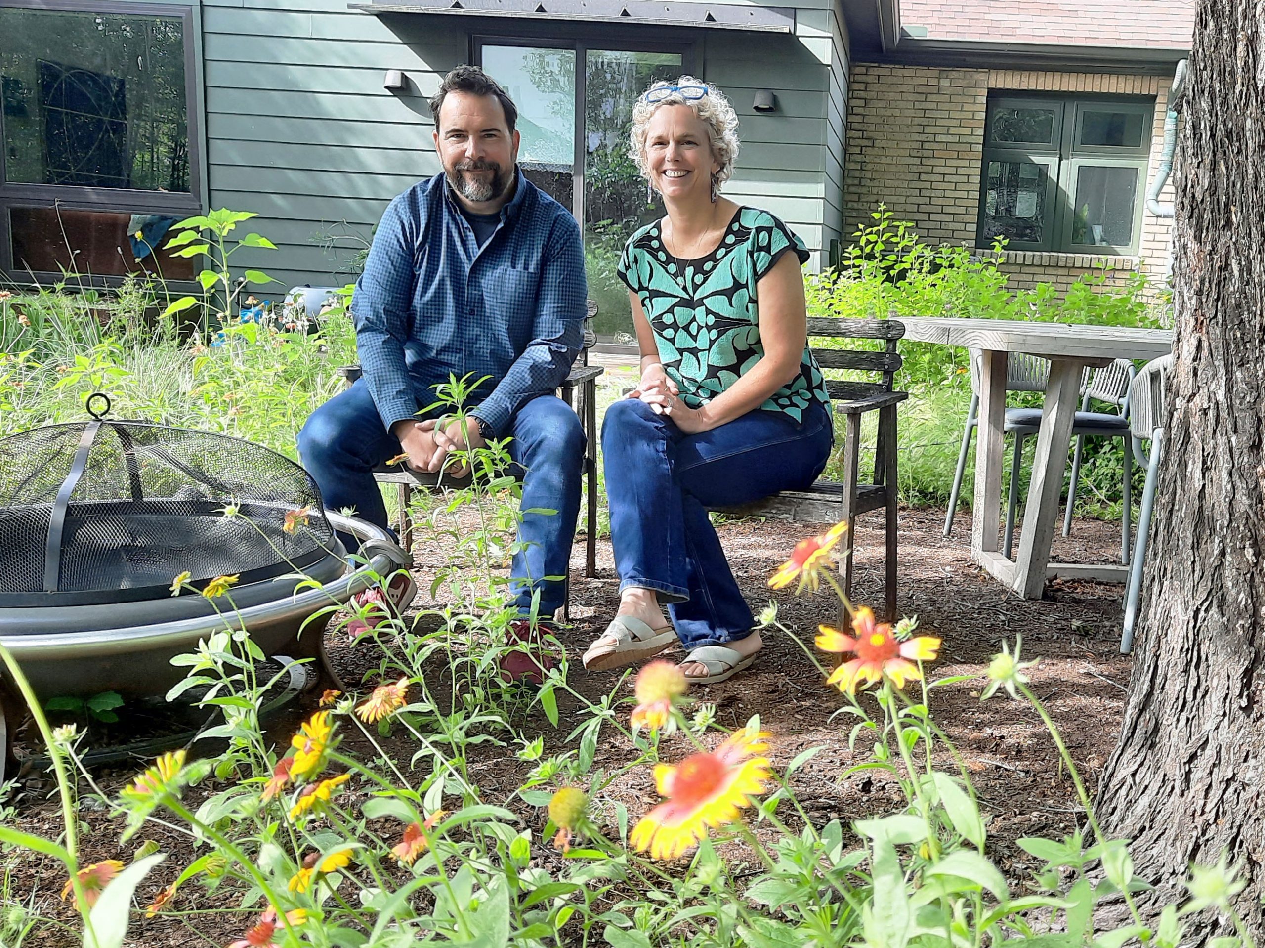 smiling man and woman in backyard with flowers and firepit 