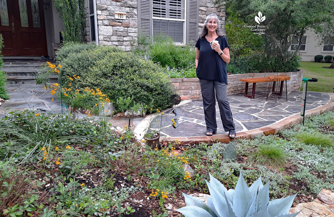 smiling woman standing on blue flagstone walkway in front of plants near front door of house 