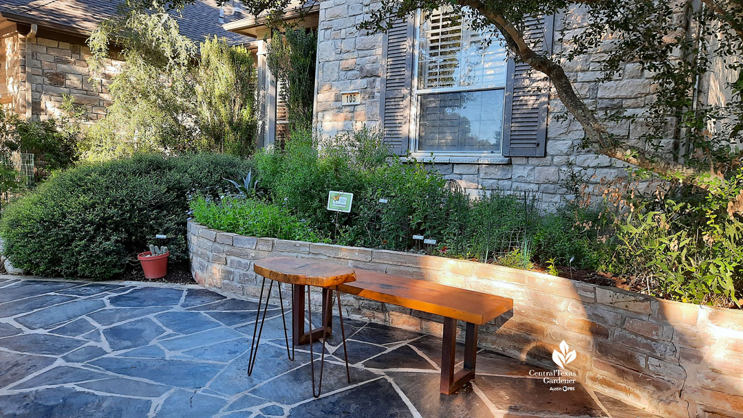 raised stone bed next to house against blue flagstone and curved wooden bench near front door 