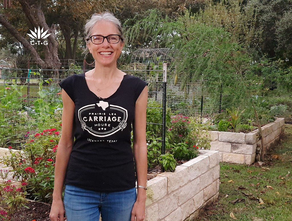 smiling woman in front of raised beds of plants