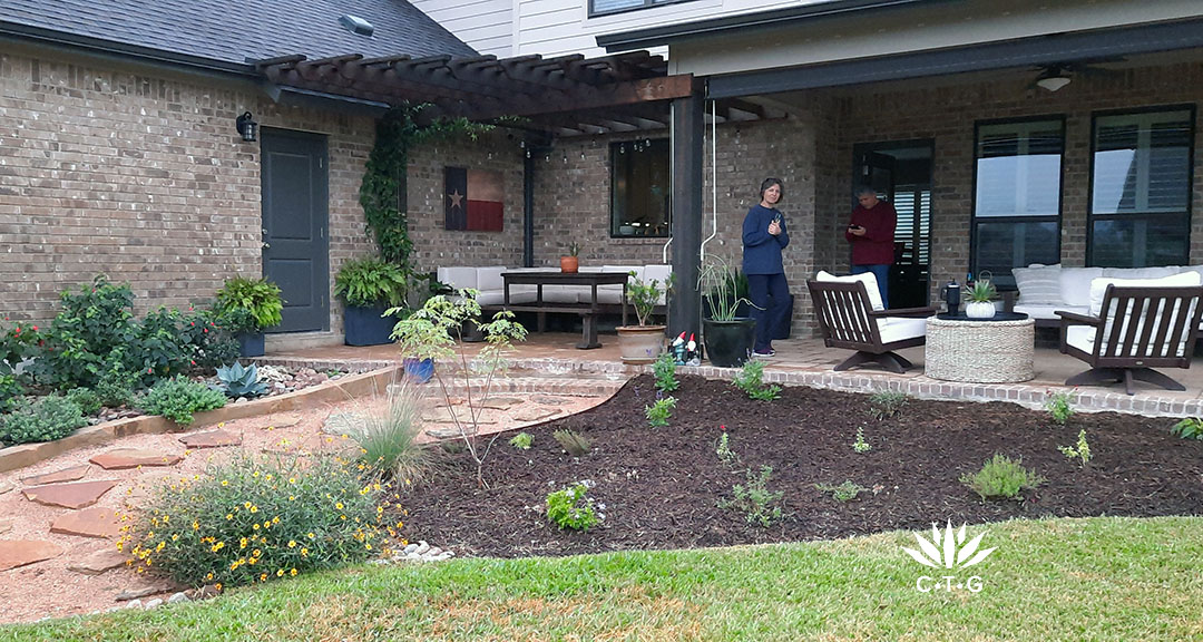 wide planting bed against lawn and wide patio with two people 