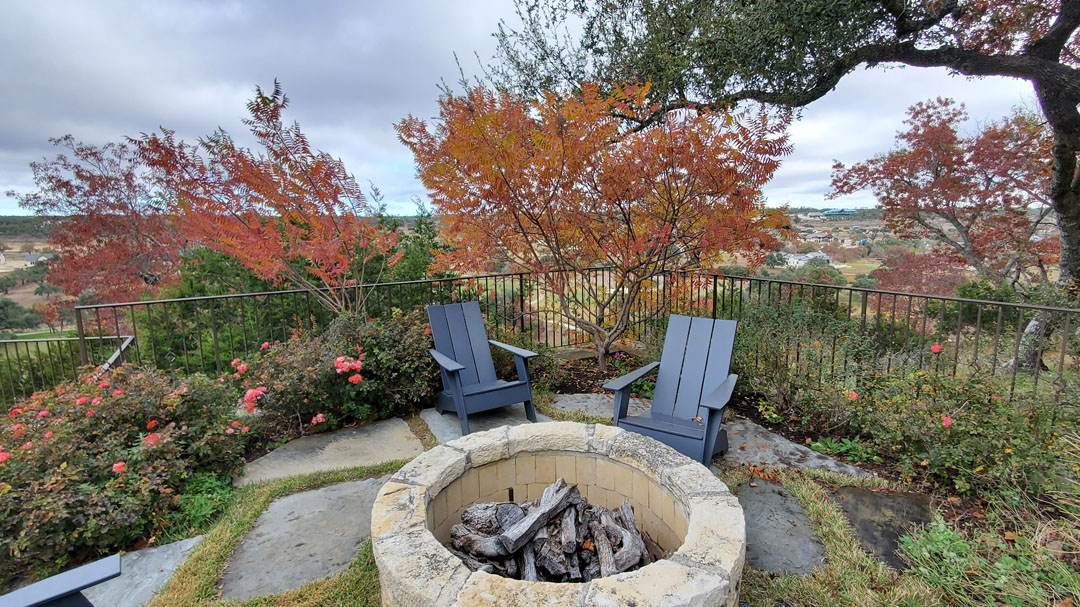 flame-colored shrub on patio with two Adirondack chairs and stone firepit 