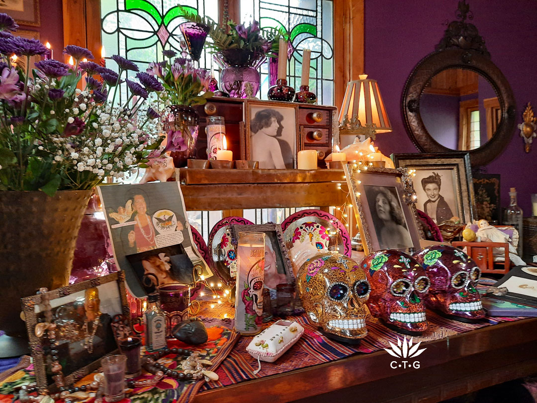 two tiered table with purple vases and candlestick holders, pictures in frames, jewelry, ornaments, and mosaic skulls 