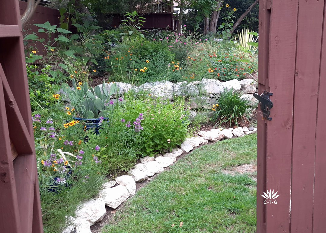 dark brown garden gate slightly open to reveal colorful garden edged by limestone rocks
