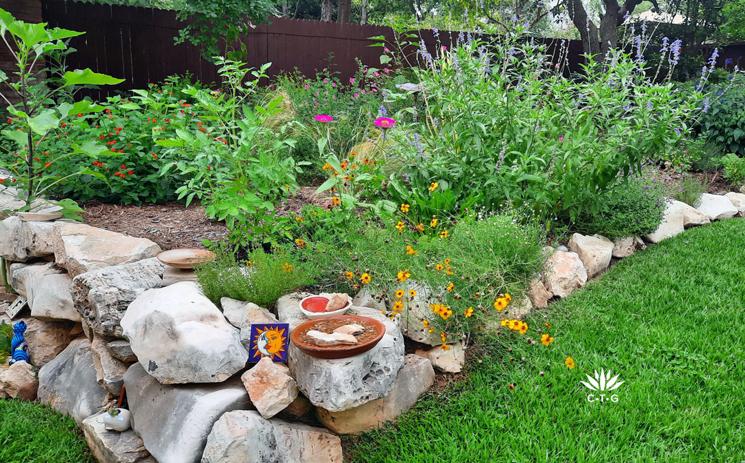 limestone-edged two level garden bed filled with colorful perennials, gold wildflowers and yellow-bordered yucca
