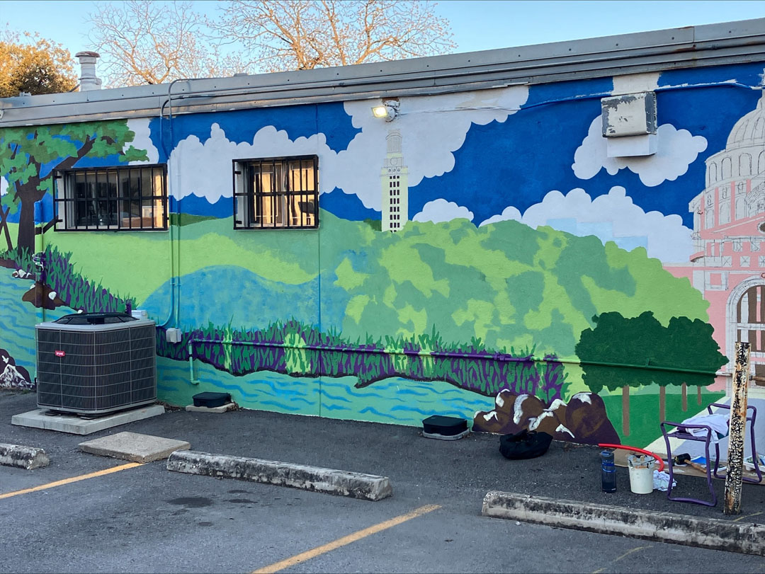 colorful landscape painting on a building wall against a parking lot