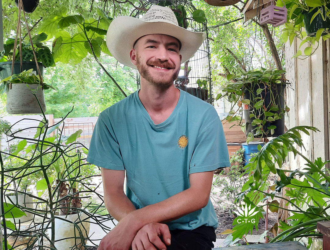 smiling young man wearing straw hat on front porch of garden 