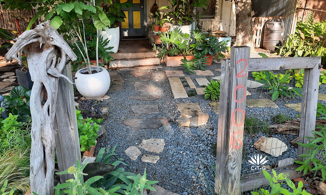 repurposed wood and tree limb entrance to small front yard; black gravel and paver path