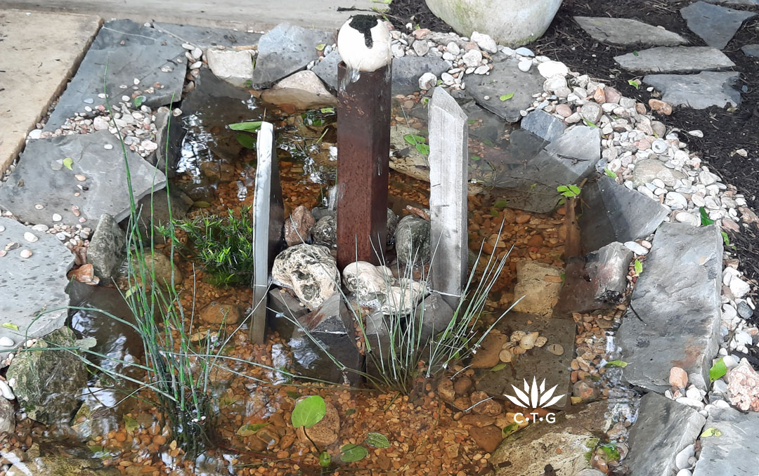 tiny pond with rusty square post topped with round ball as fountain