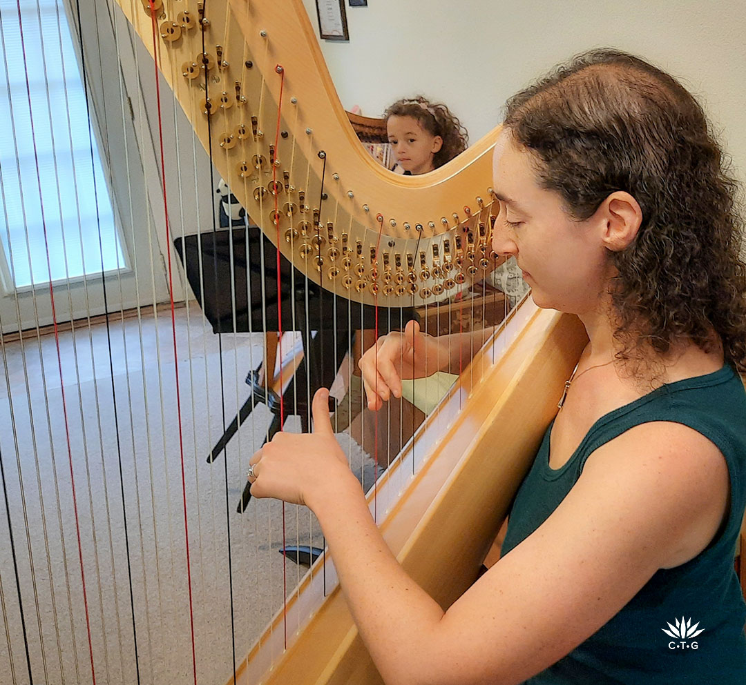 woman playing harp while daughter looks on 