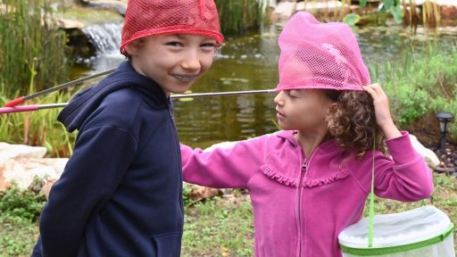 two young children playing with butterfly nets on their heads in their backyard