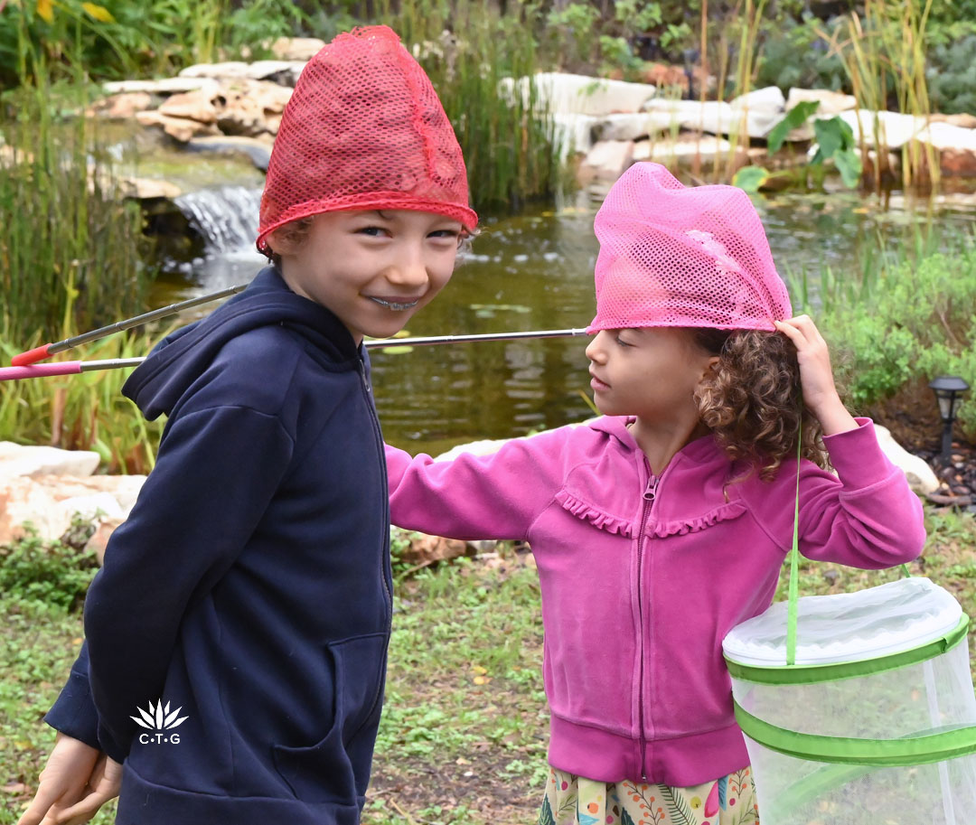 two young children playing with butterfly nets on their heads in their backyard 