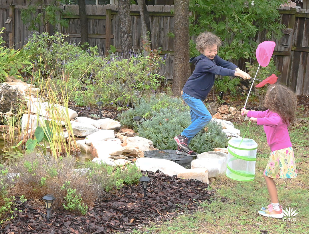 young boy and girl playing with butterfly nets and jumping from limestone border of pond 